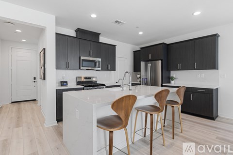 A kitchen with black cabinets and a white island with three chairs.