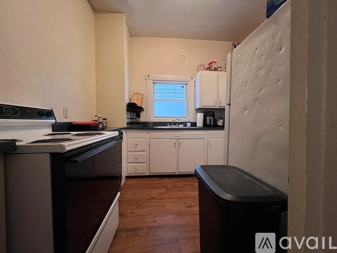 A kitchen with white cabinets and a black trash bin.