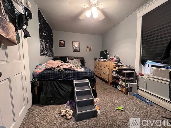 A room with a bed, a desk, and a ceiling fan.