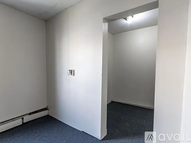 A room with a carpeted floor and a white wall with a doorway leading to another room.