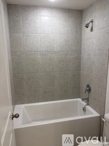 A white bathtub in a bathroom with grey tiles.