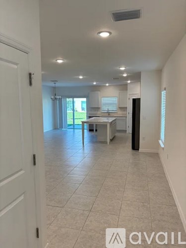 A spacious room with tiled flooring and a kitchen area in the background.