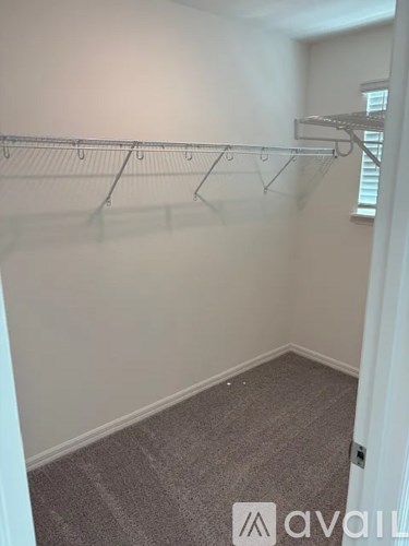 A room with a grey carpet and a white wall with a clothes rack.