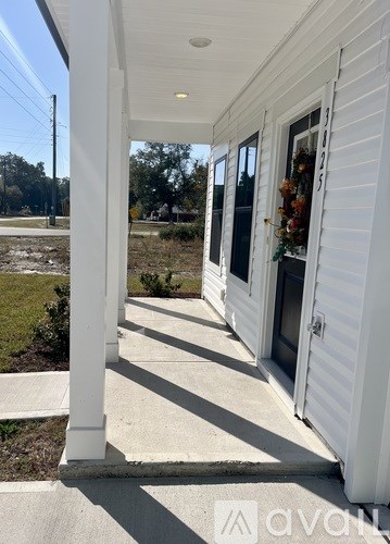 A white house with a porch and a door decorated with wreaths.