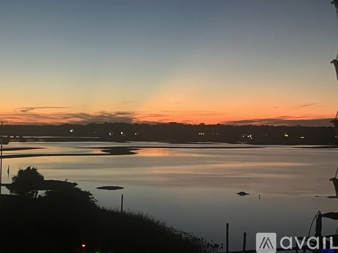 A sunset view over a calm body of water with a few boats and a tree silhouette.