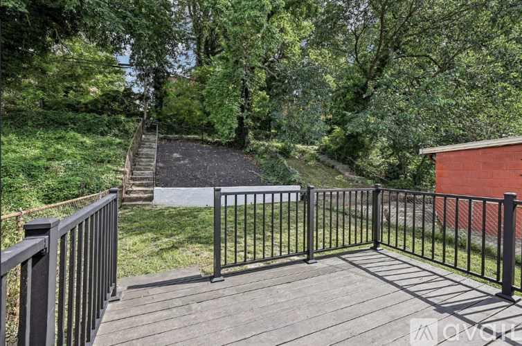 A wooden deck with a black railing overlooks a grassy area and a small building.