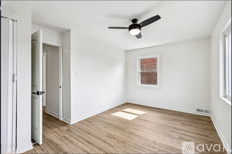 A room with a ceiling fan and a window with a brick wall behind it.