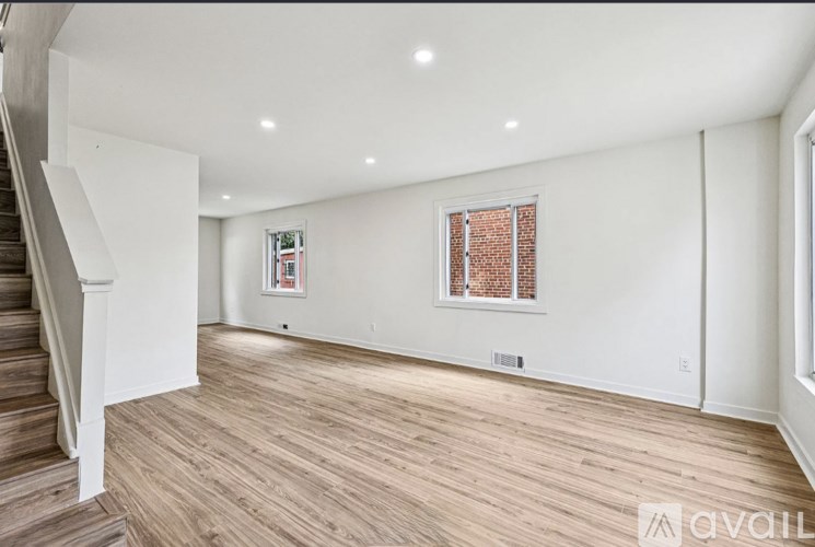 A spacious room with wooden flooring and a staircase on the left side.