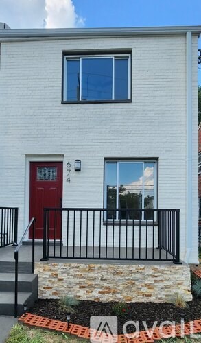 A white house with a red door and a black railing.