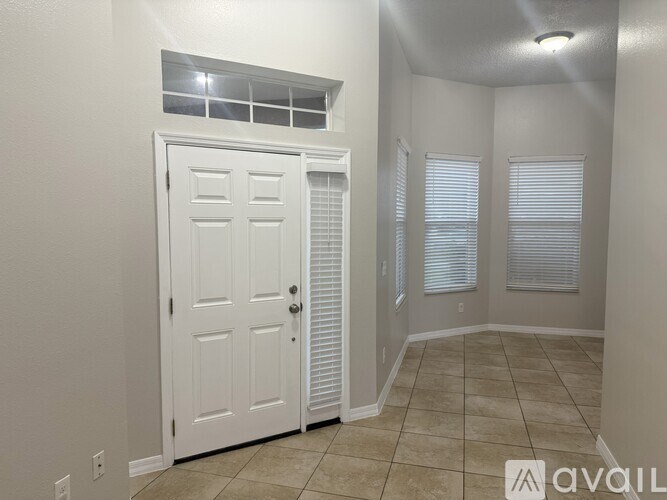 A white door is in a room with tiled flooring and a window with blinds.