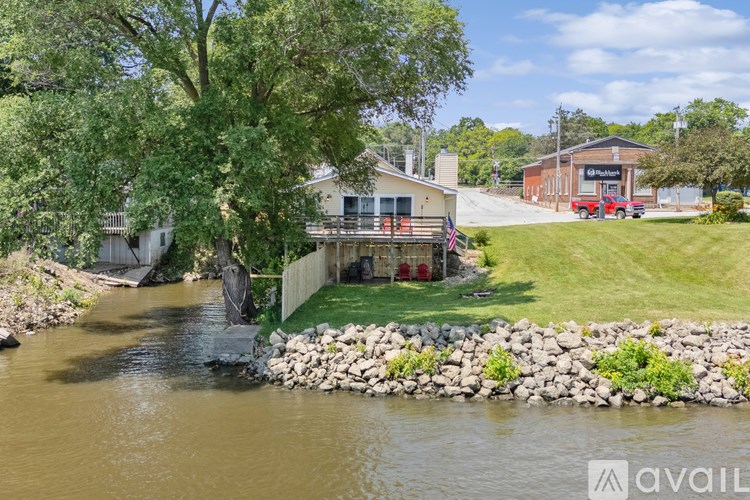 A house with a flag on the front porch is surrounded by a grassy area and a river.