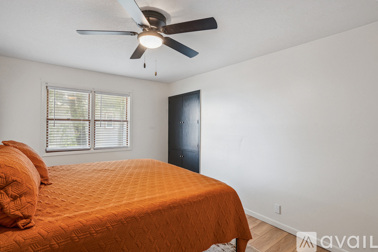 A bedroom with a bed, ceiling fan, and a window with blinds.