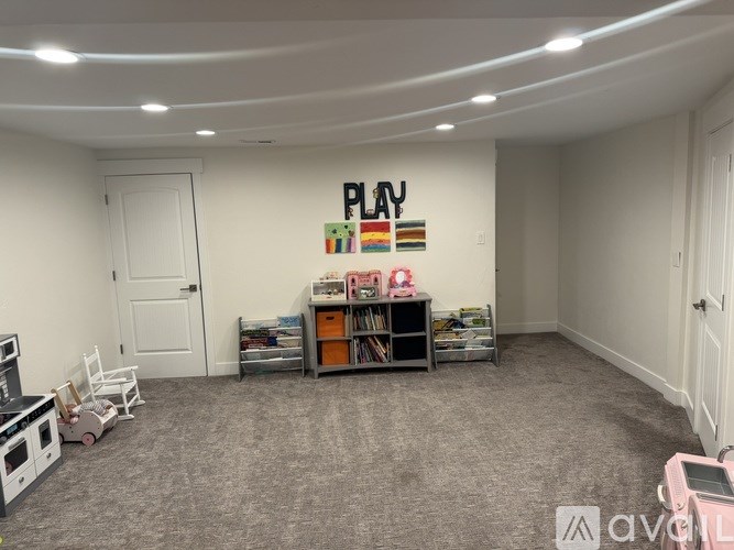 A room with a grey carpet and a white door with a sign that says "PLAY" on the wall.