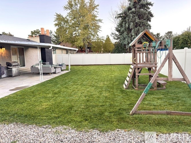 A backyard with a wooden swing set and a gravel area in the foreground.