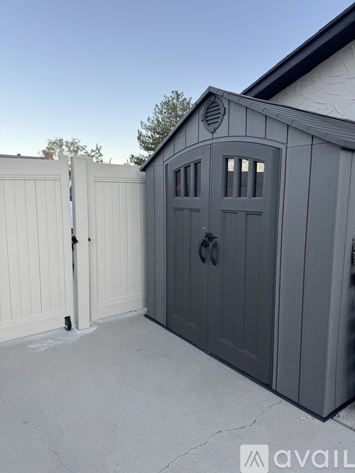 A grey shed with a white fence in front of it.