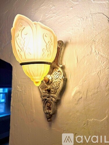 A wall mounted light fixture with a white shade and ornate design.