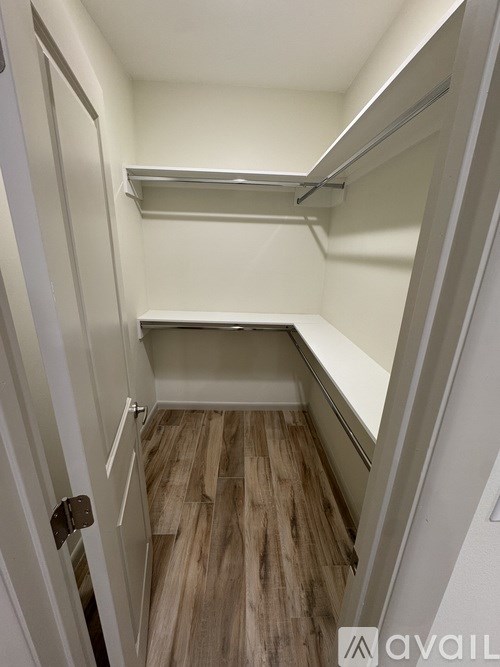 A white door with a handle is open to a small, empty room with a wooden floor.