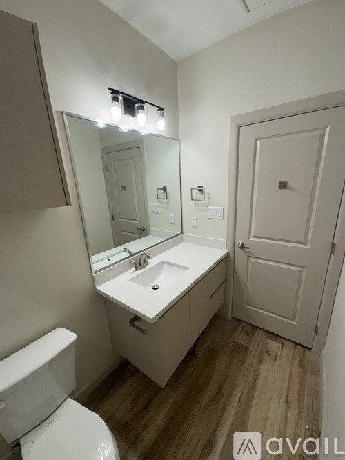 A bathroom with a toilet, sink, mirror, and wooden floors.