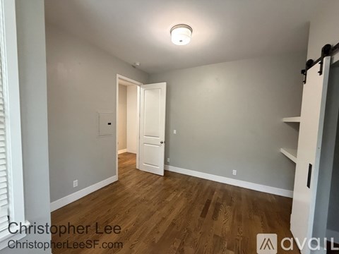 A room with wooden floors and white walls, with a doorway leading to another room.