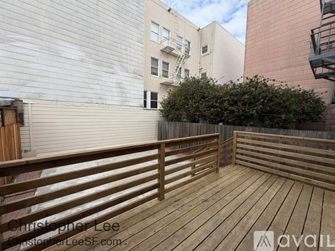 A wooden deck with a railing and a building in the background.