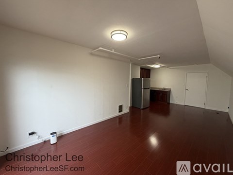 A room with wooden floors and white walls, with a ceiling light and a door on the right side.
