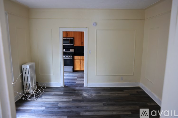 A room with a wooden floor and a white wall with a doorway leading to another room.