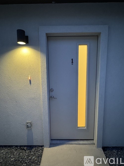 A white door with a number 1 on it is illuminated by a light on the wall.