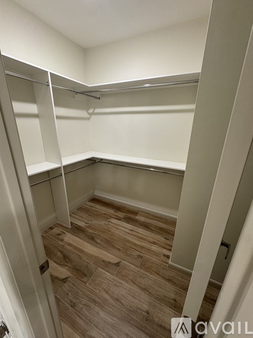 A walk-in closet with wooden floors and white shelving.