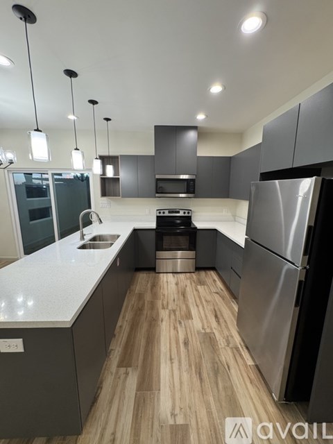 A modern kitchen with a stainless steel refrigerator and wooden flooring.