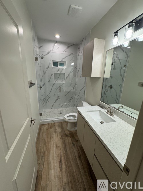 A bathroom with a marble shower and wooden floors.