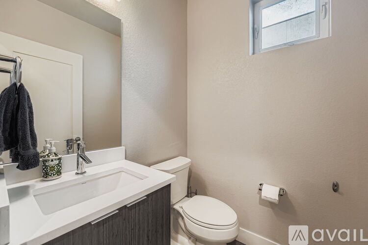 A bathroom with a toilet, sink, mirror, and a towel hanging on the door.