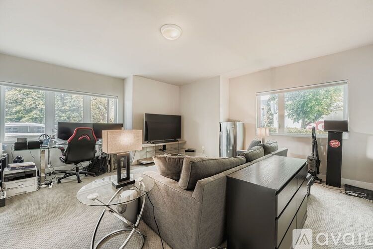 A modern living room with a grey couch, a black chair, a television, and a desk with a computer.