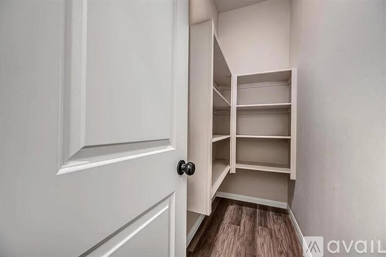 A white door opens to a small, empty room with a wooden floor.