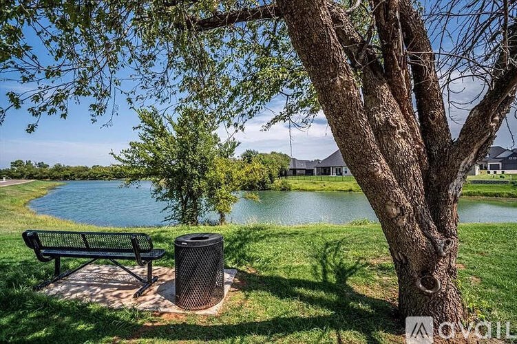 A park bench is situated under a tree next to a lake.
