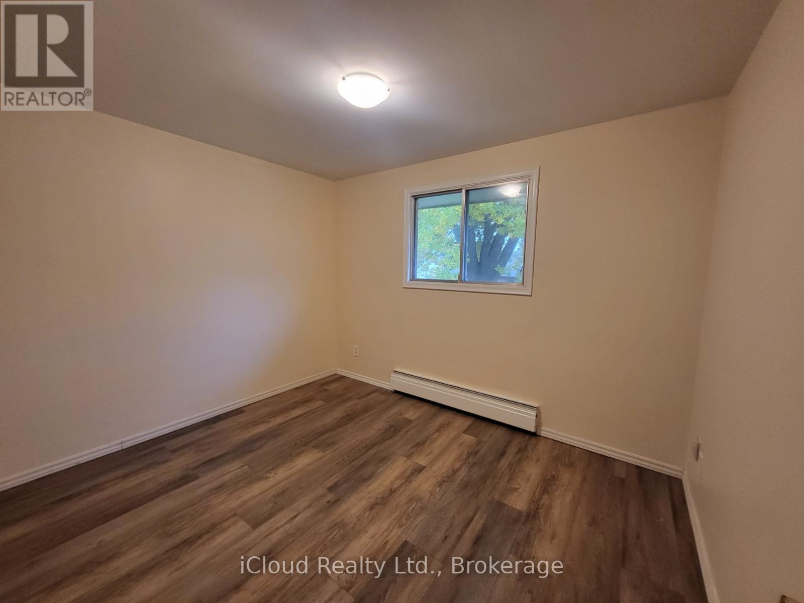 A room with wooden flooring and a window showing trees outside.