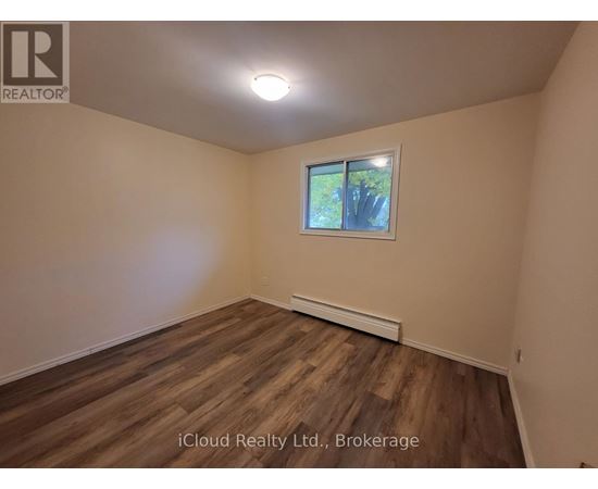 A room with wooden flooring and a window showing trees outside.