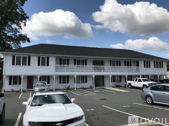 A white car is parked in a parking lot in front of a white building with a black roof.