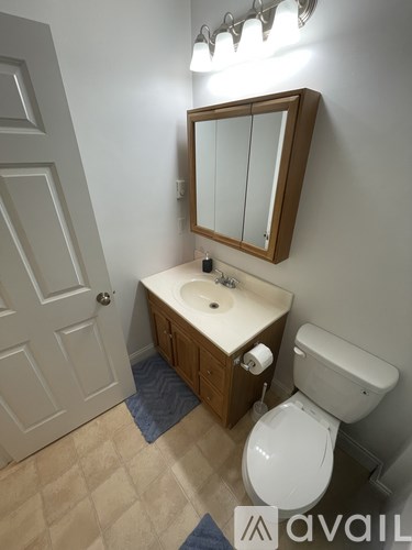 A bathroom with a toilet, sink, mirror and light.