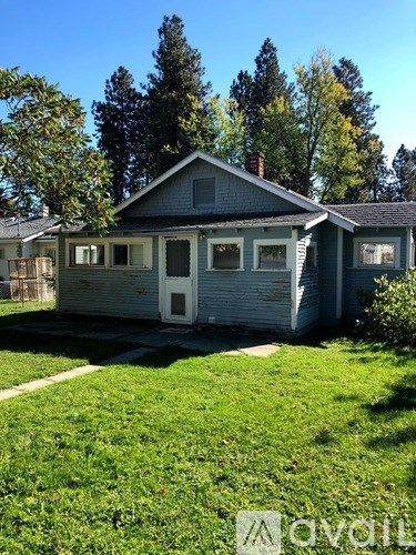 A house with a white door and a grey roof is surrounded by green grass and trees.