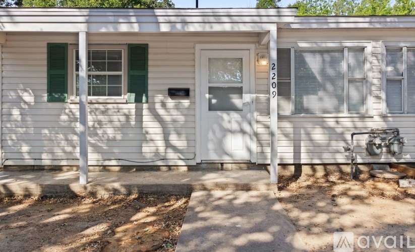 A white house with a grey door and green shutters.