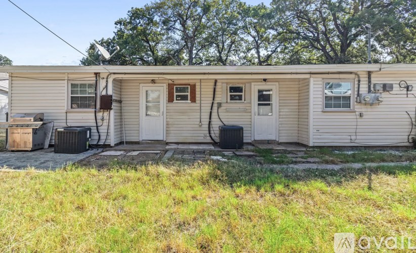 A mobile home with a white door and windows, surrounded by grass and trees.