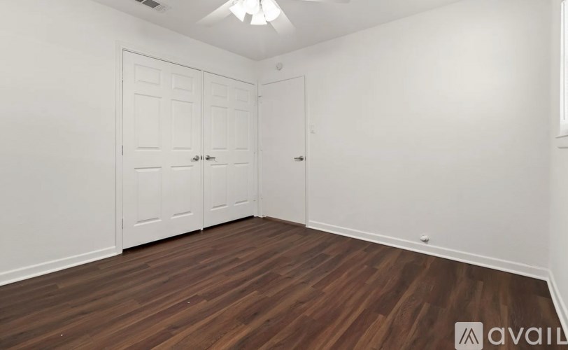 A room with white walls and wooden flooring, featuring a set of white doors.