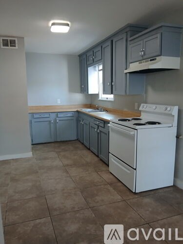 A kitchen with a white stove top oven and grey cabinets.