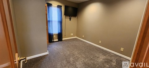 A room with a carpeted floor and a flat screen TV mounted on the wall.