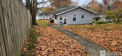 A house with a grey roof is surrounded by a fence and a path of fallen leaves.