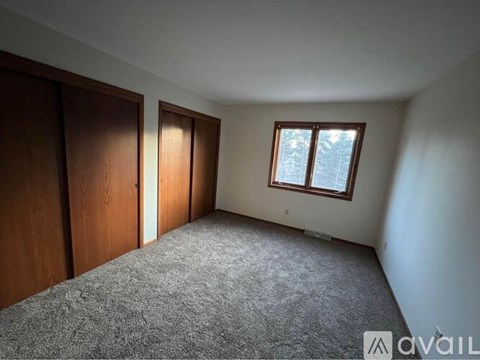 A room with a carpeted floor, two doors, and a window with a view of trees outside.