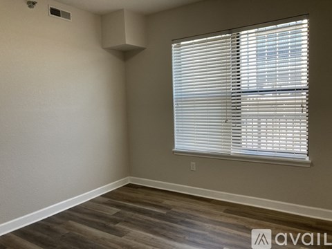 A room with a window covered by white blinds and a wooden floor.