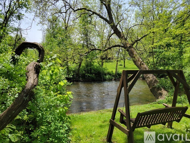 A wooden bench sits in front of a river with a tree branch arching over it.