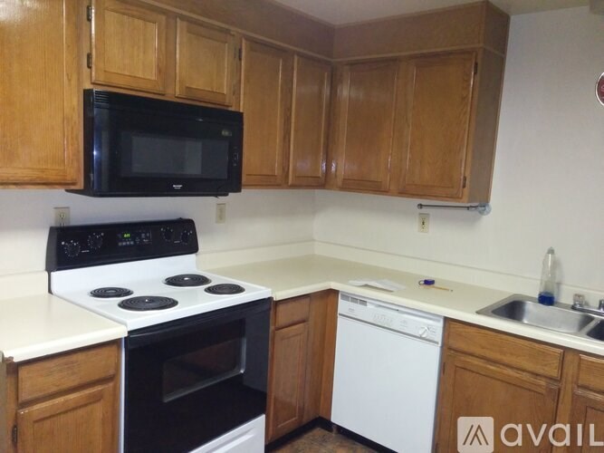 A kitchen with a black microwave above a stove and wooden cabinets.