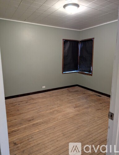 A room with wooden flooring and a window with closed blinds.